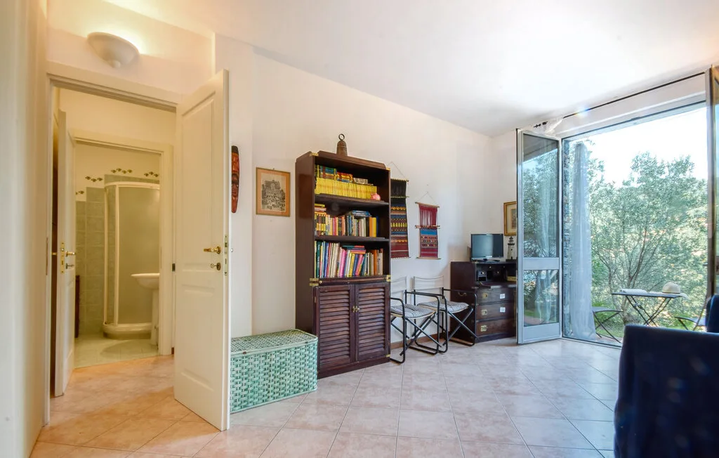 Una habitación luminosa con una estantería y puertas de vidrio abiertas hacia la vegetación.