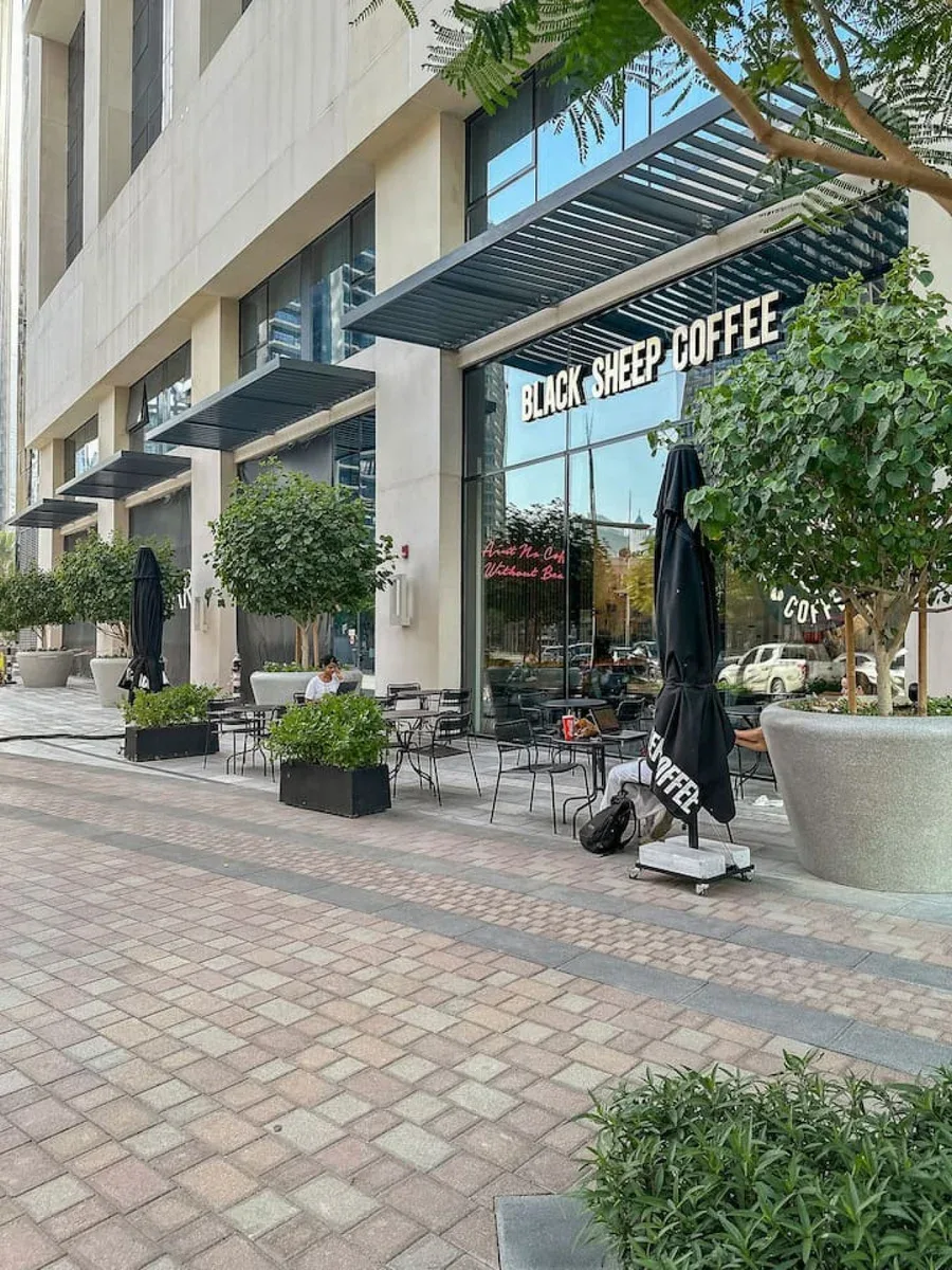 Una cafetería a pie de calle con mesas al aire libre y plantas en macetas.
