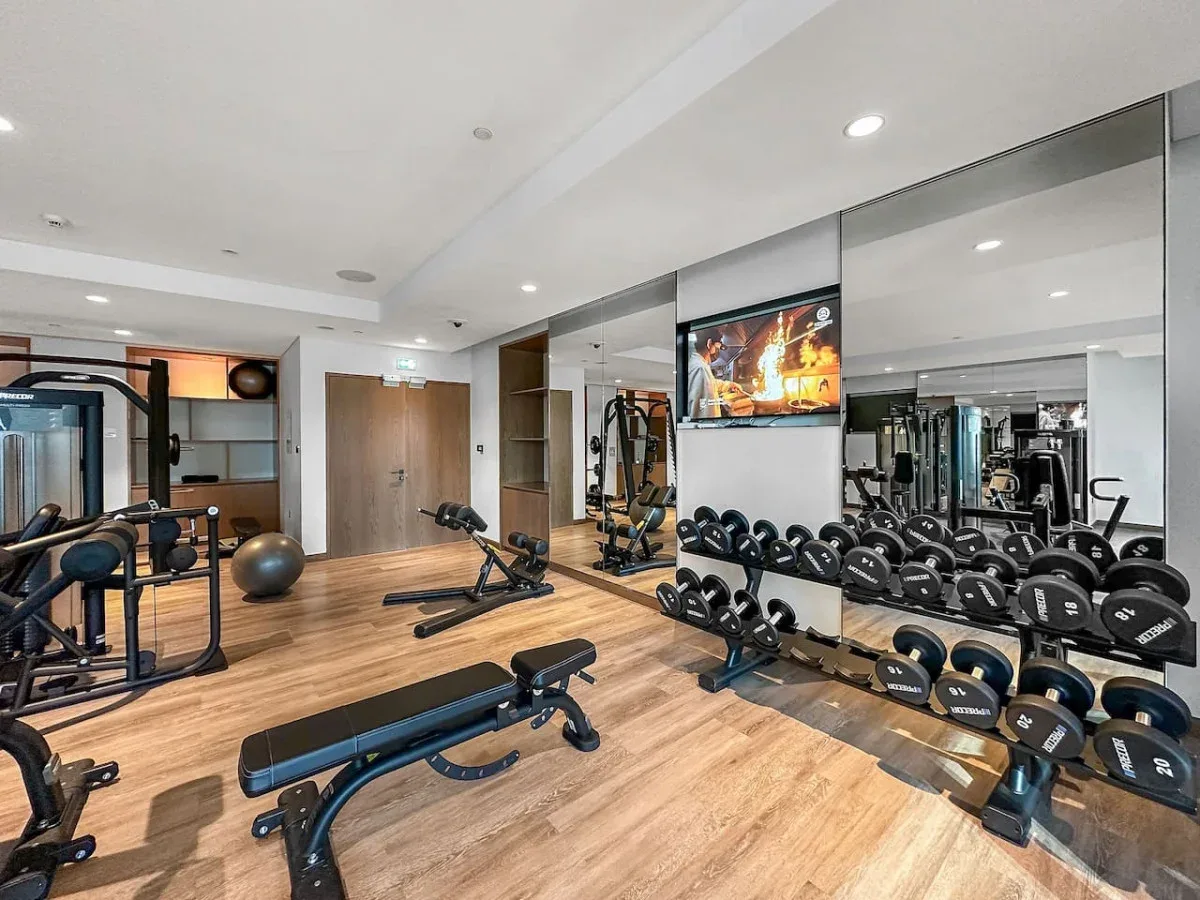 Un gimnasio con bancos de pesas, mancuernas y equipo de ejercicio reflejado en un espejo.