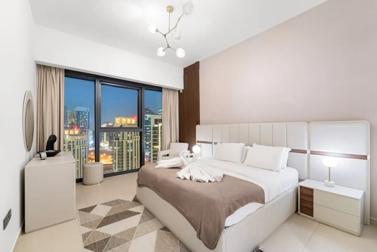 Un dormitorio con una cama grande junto a ventanales con vistas a las luces de la ciudad.