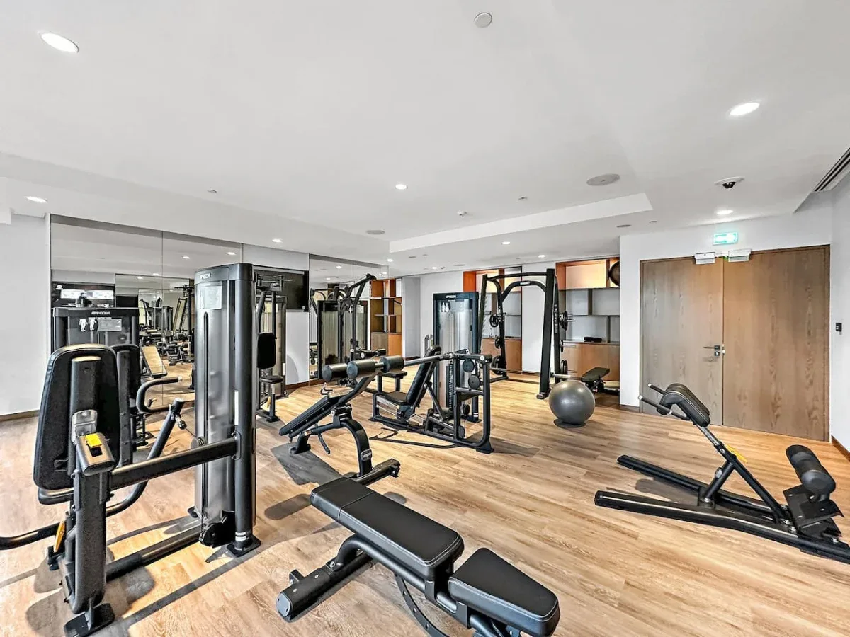 Un gimnasio con máquinas de ejercicio y bancos distribuidos por la sala.