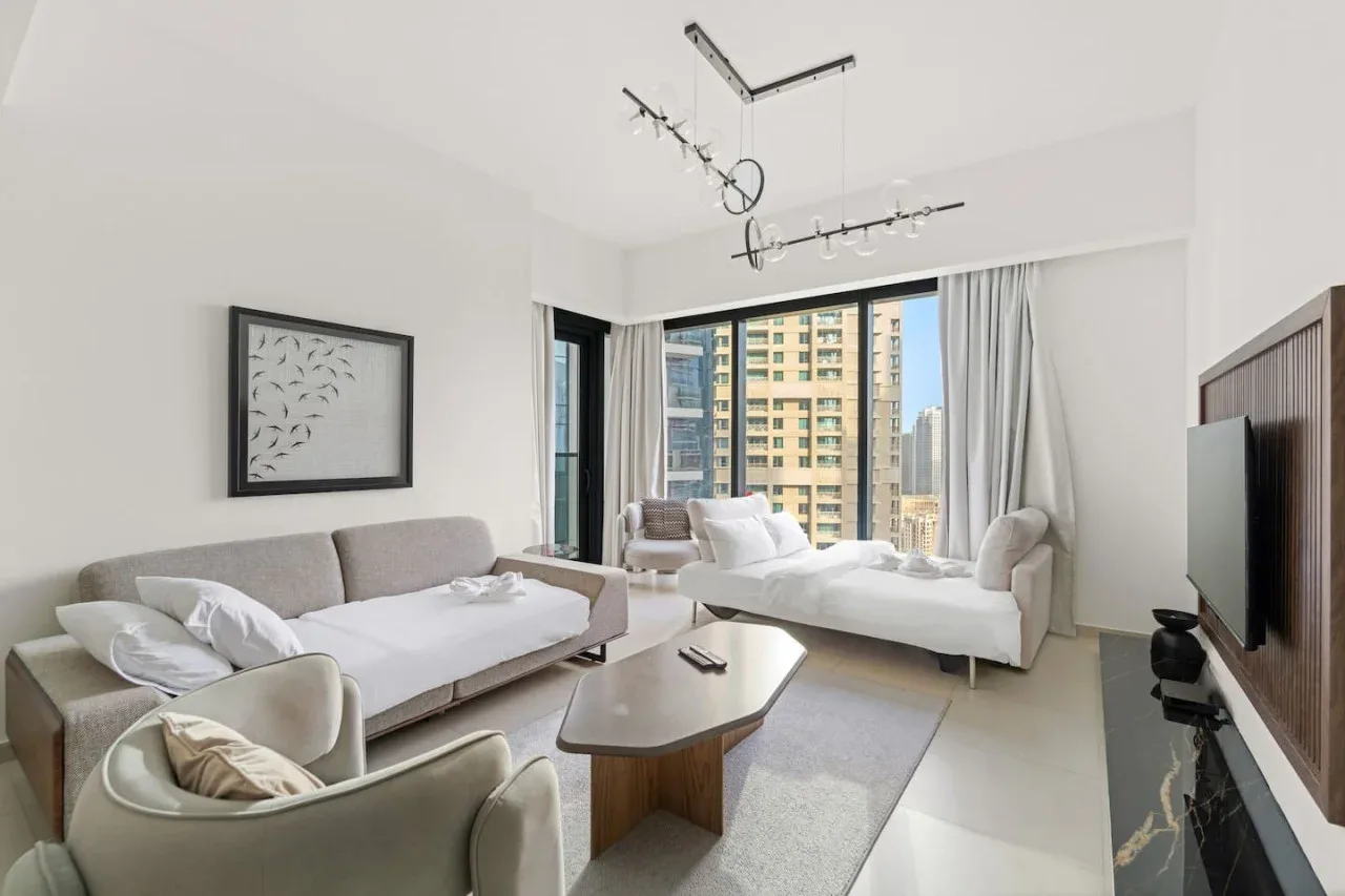 Una sala luminosa con un sofá y una cama de día junto a grandes ventanales.