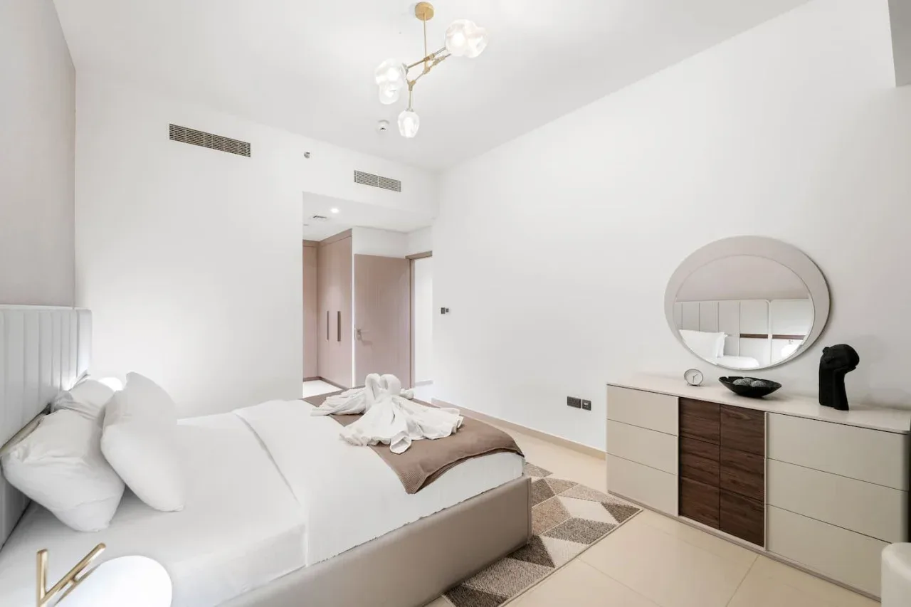 Un dormitorio luminoso con una cama, una cómoda y un espejo redondo.
