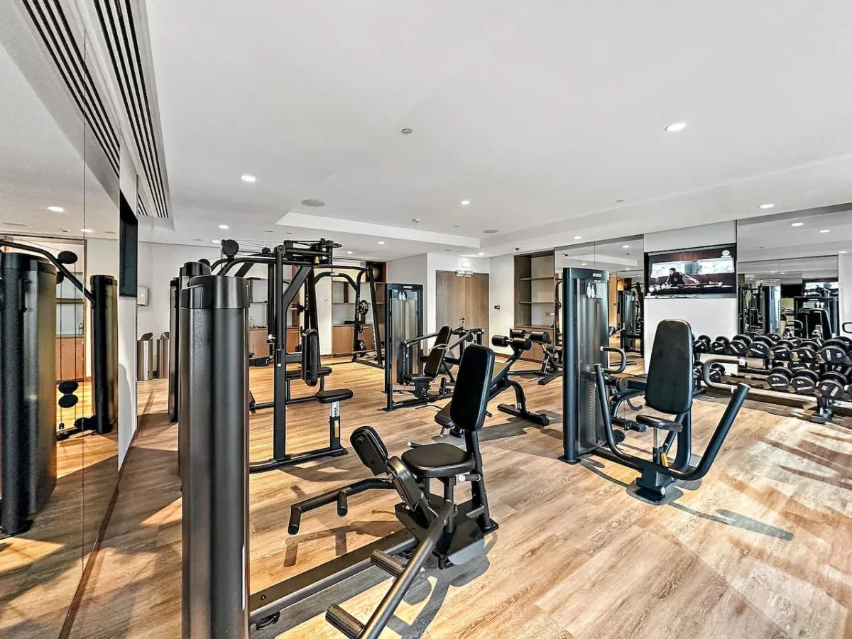 Un gimnasio con máquinas de ejercicio y pesas sobre un suelo de aspecto madera.