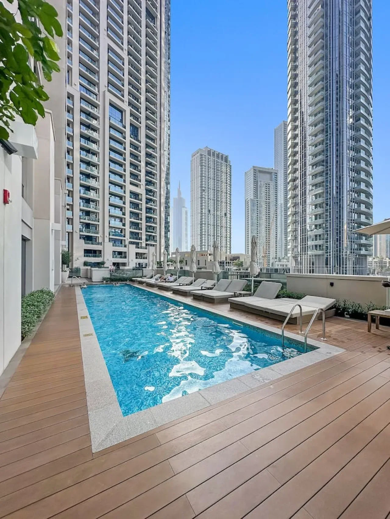 An outdoor swimming pool sits on a wooden deck among tall city buildings.