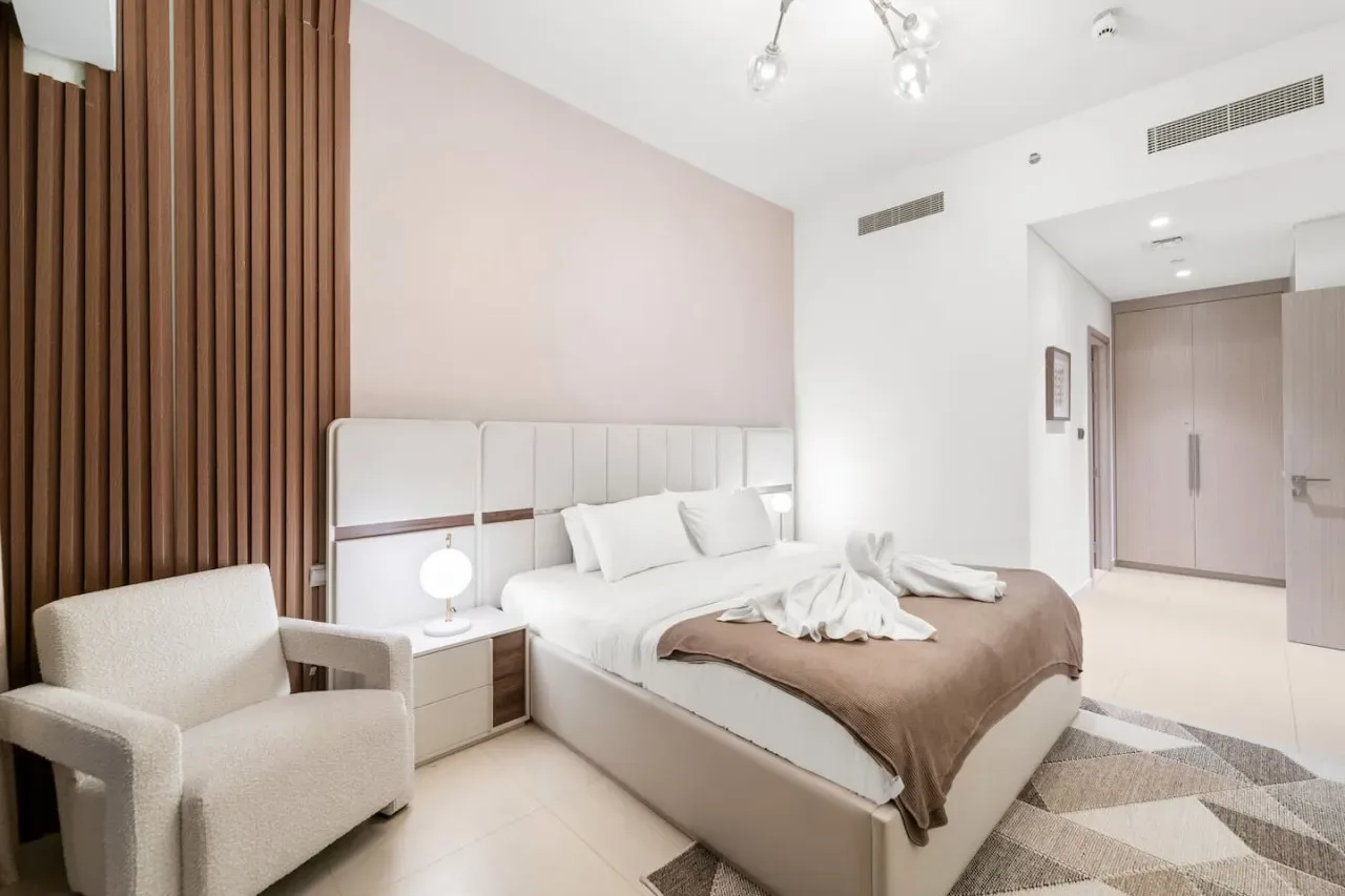 A bedroom with a neatly made bed and an upholstered armchair.