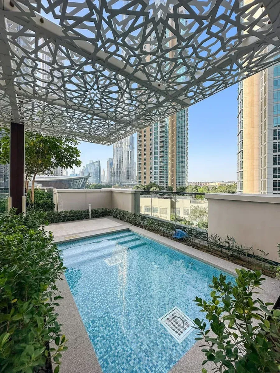 Una piscina en la azotea está bajo una cubierta calada, con edificios altos al fondo.