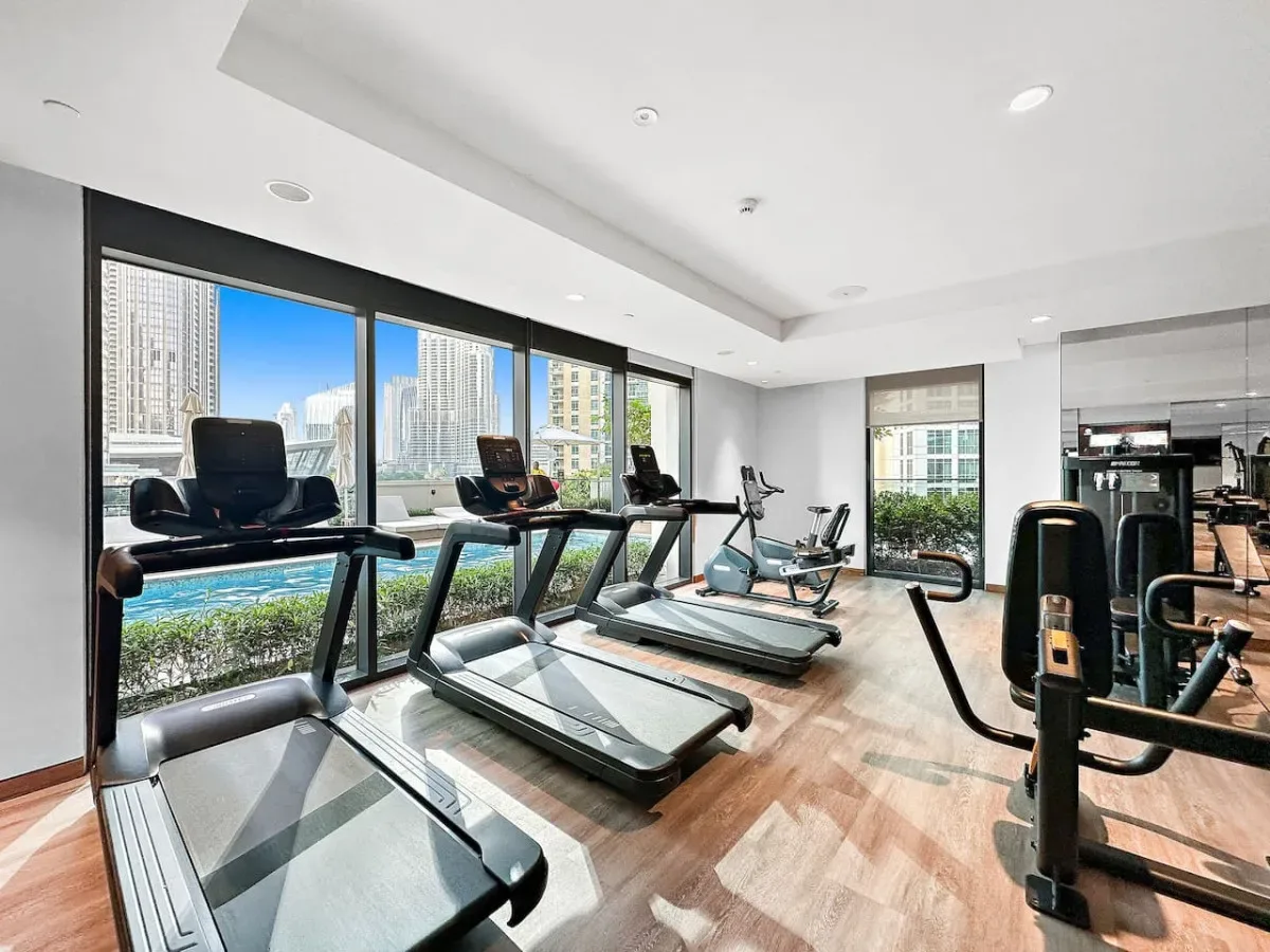 Un gimnasio luminoso con cintas de correr y máquinas de ejercicio junto a grandes ventanas.