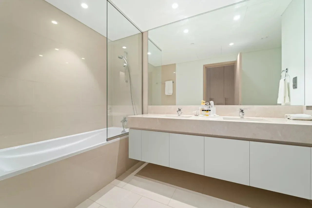 Un baño luminoso con bañera, mampara de vidrio y un amplio lavabo.