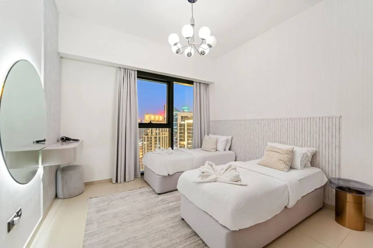 Un dormitorio luminoso con dos camas junto a una gran ventana con vistas a las luces de la ciudad.