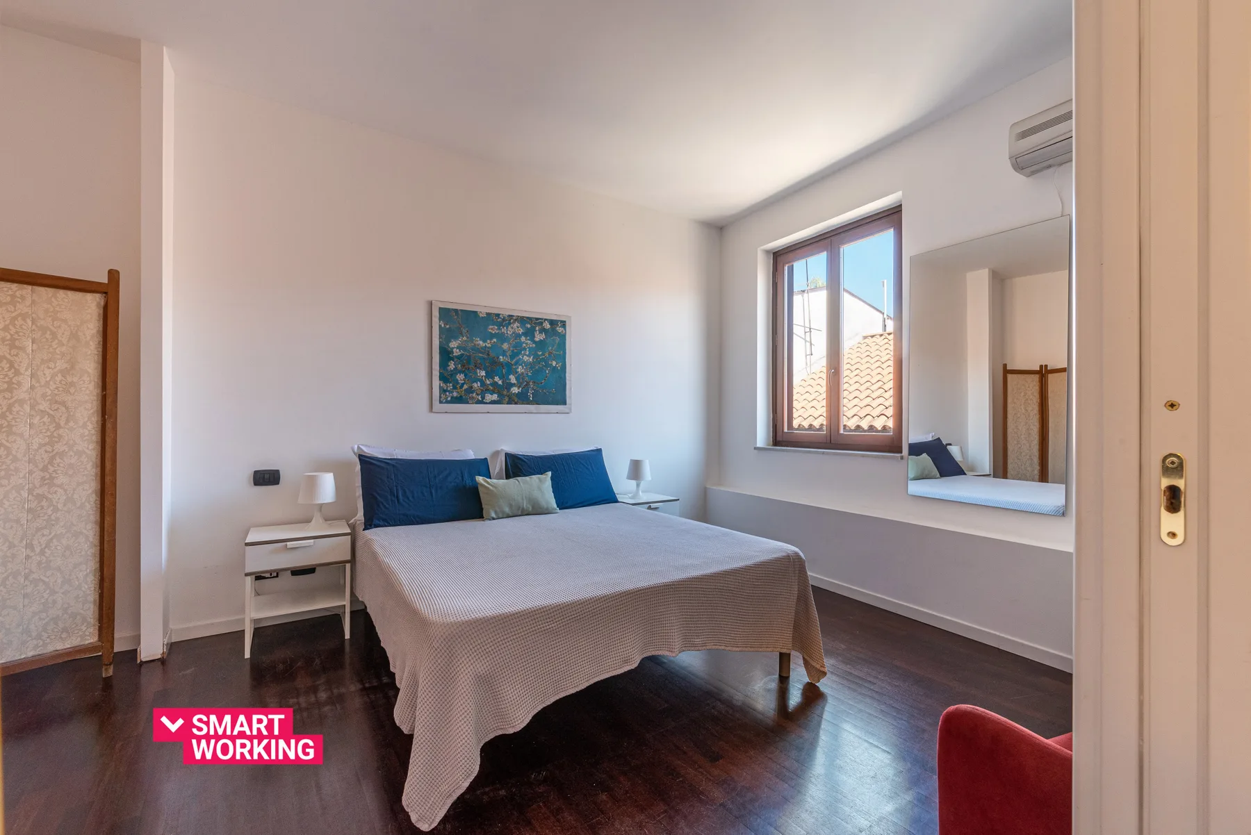 Un dormitorio con una cama, una mesita de noche y una ventana con tejados a la vista.