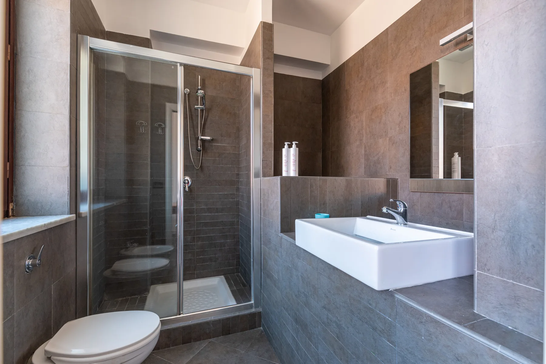Un baño moderno con una ducha de vidrio y un lavabo montado en la pared.
