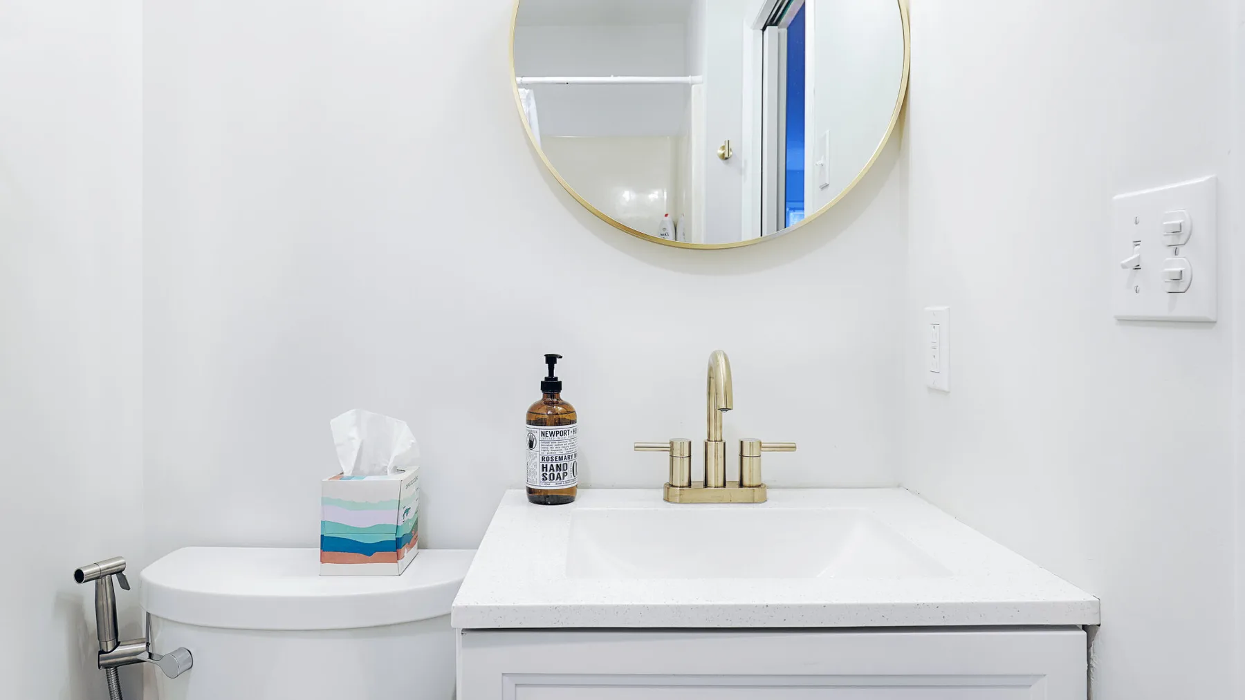 A bathroom vanity with a sink, gold-tone faucet, and round mirror.