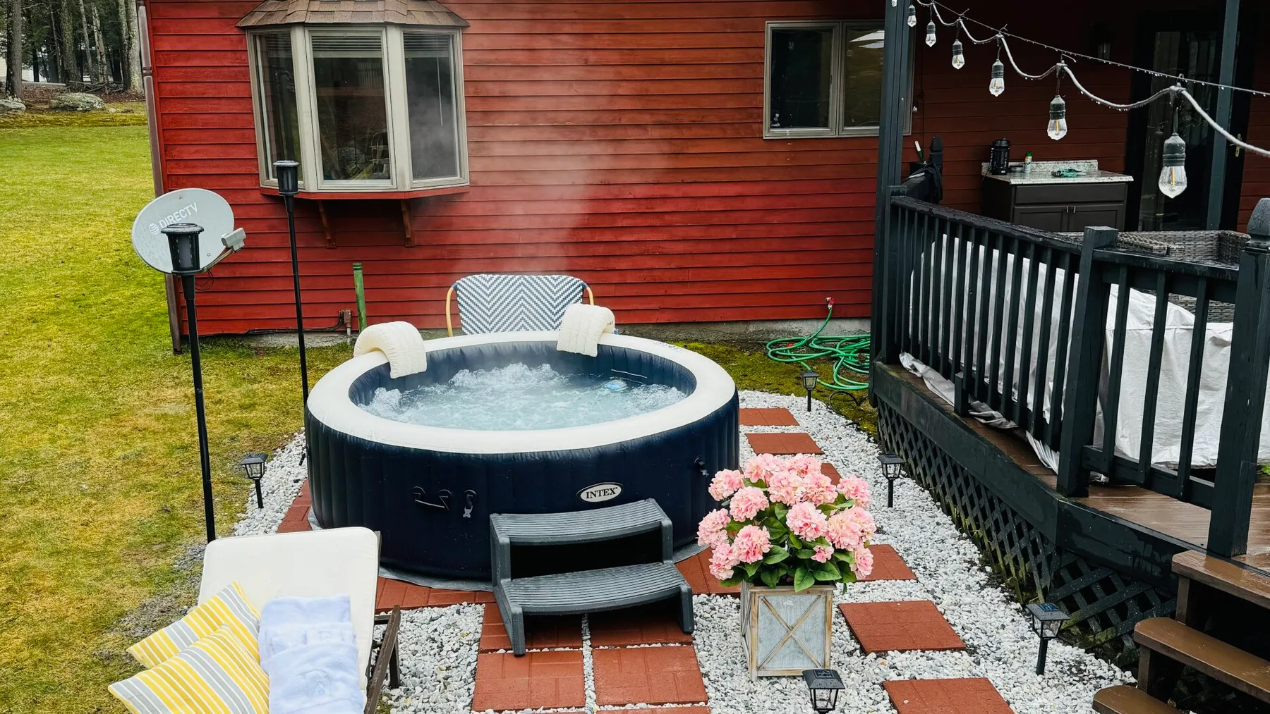 A bubbling outdoor hot tub sits beside a red-sided building and raised deck.