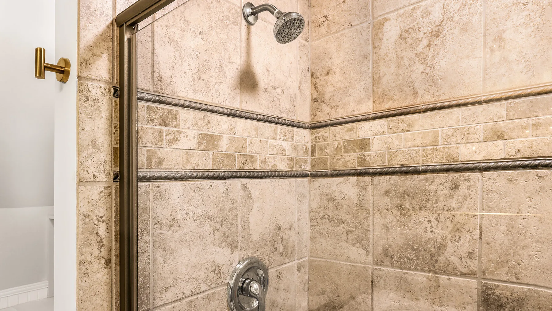 A tiled shower with a metal showerhead and wall controls.