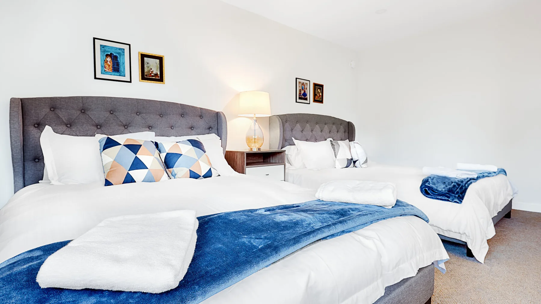 A bright bedroom with two beds dressed in white linens and blue accents.