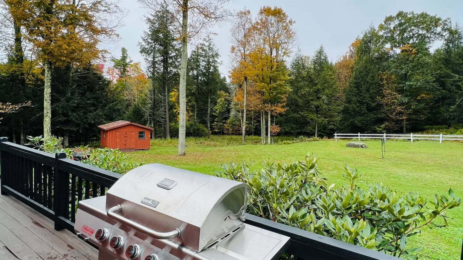 An outdoor deck overlooks a grassy yard, with a stainless-steel grill in the foreground.