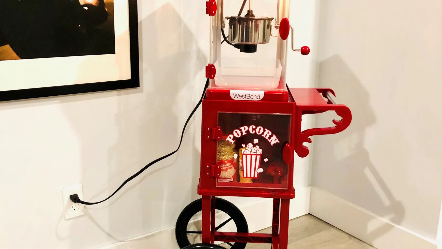 A red popcorn machine stands against a light-colored wall.