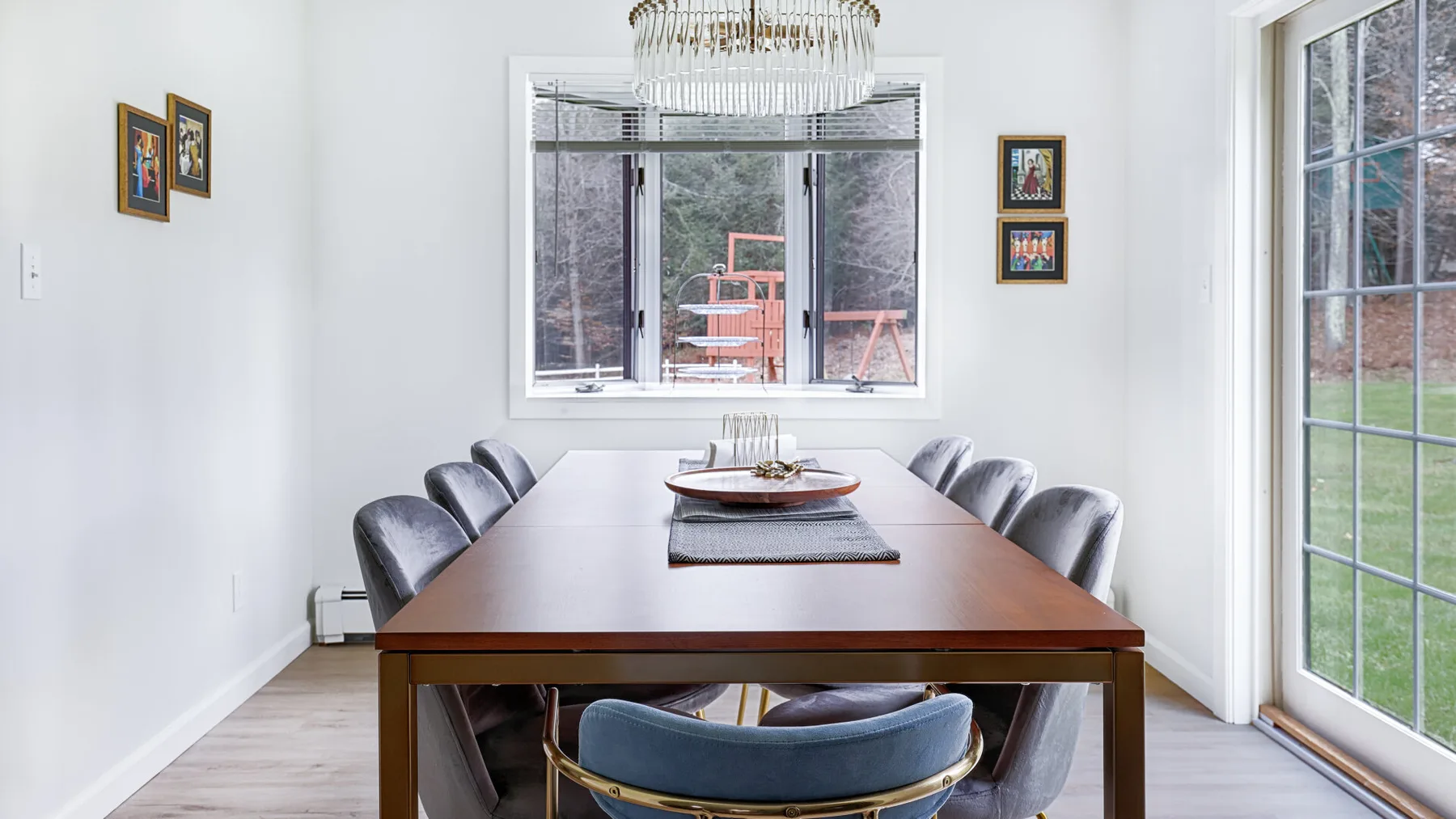 A bright dining room with a long table, upholstered seating, and large windows.