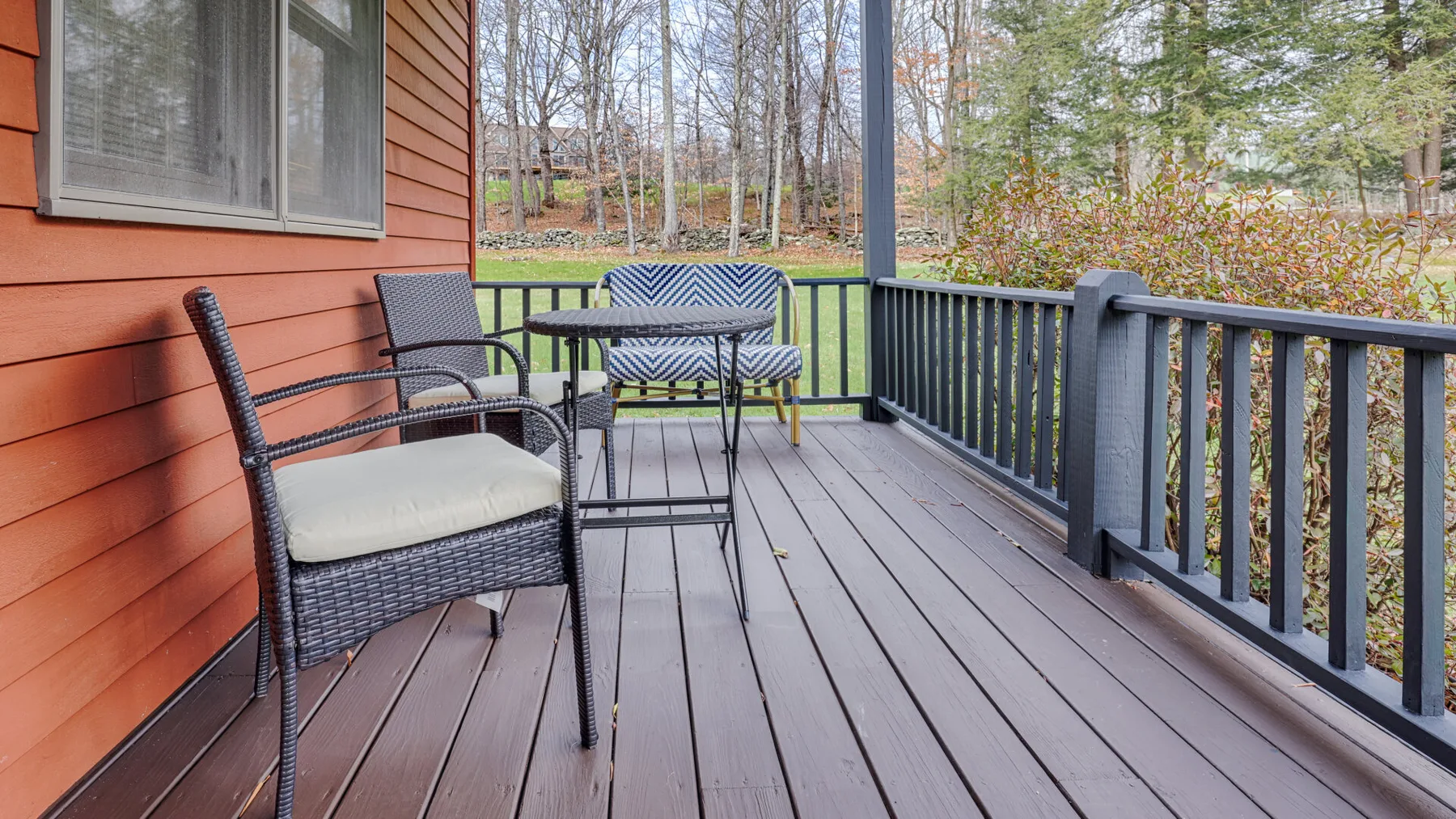 A wooden deck with outdoor seating overlooks a wooded yard.