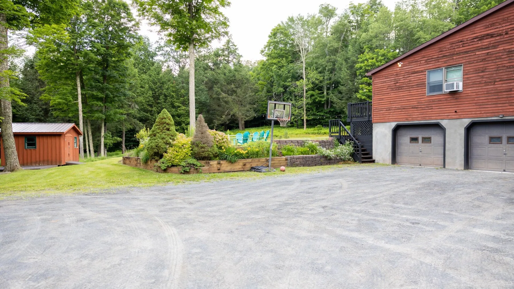 A paved driveway beside a red-sided building, with a basketball hoop and trees.