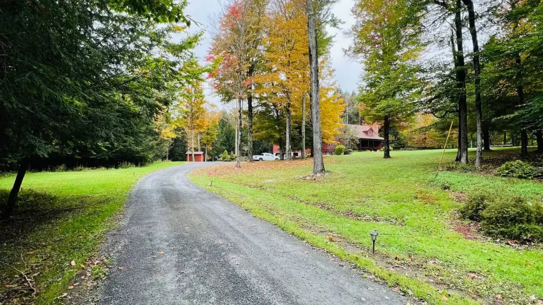 A curved driveway passes through a grassy, tree-lined landscape.