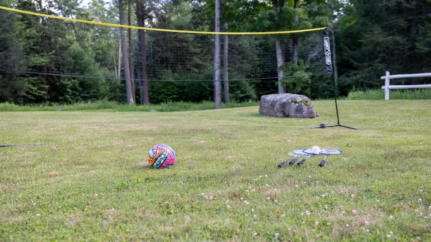 A grassy outdoor area has a volleyball net and several balls.