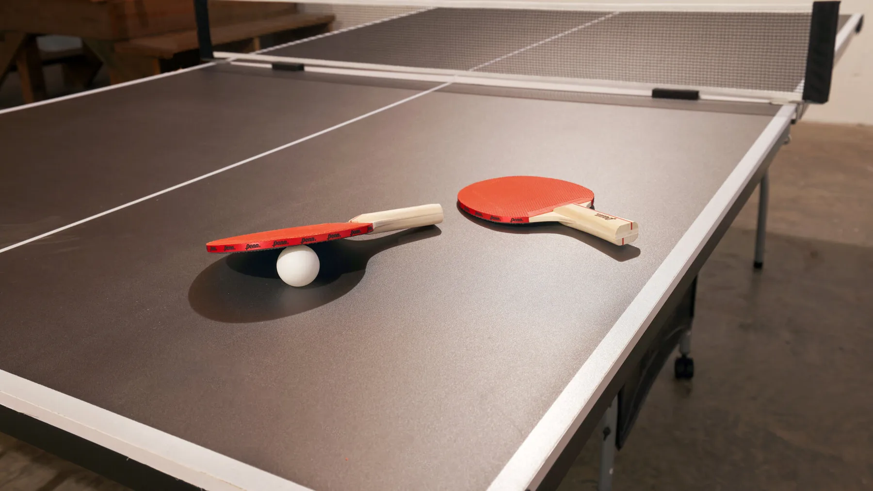 A table tennis table with paddles and a ball rests in an indoor recreation area.