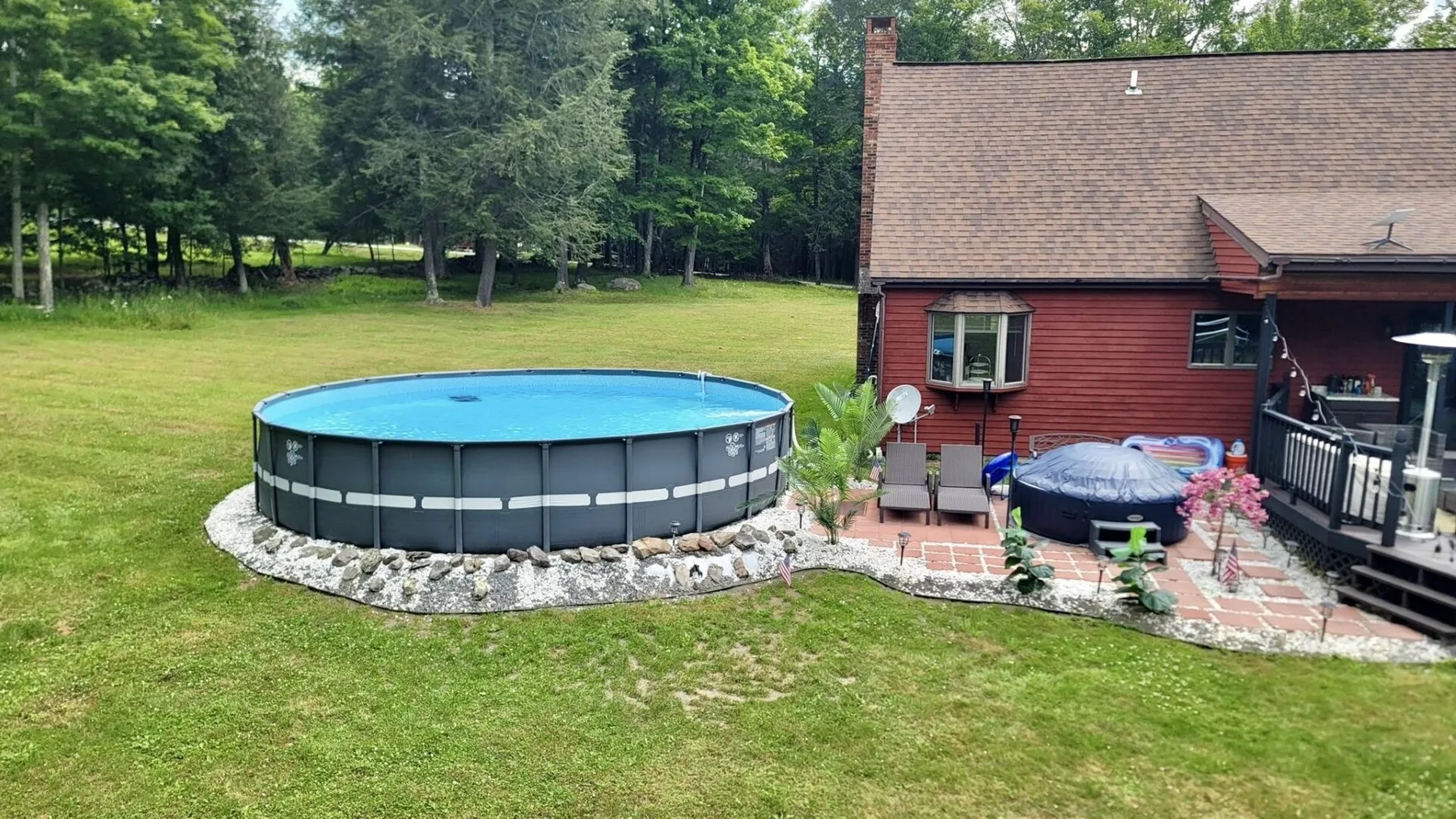 A backyard with an above-ground pool beside a red house.
