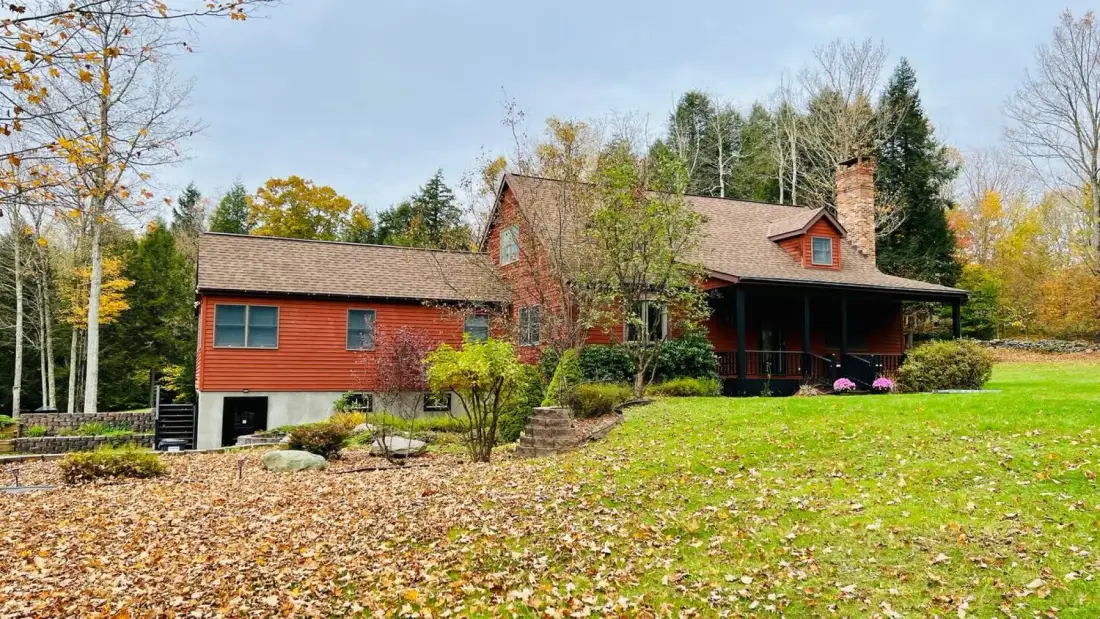 A red house sits beside a broad green lawn and leafy trees.