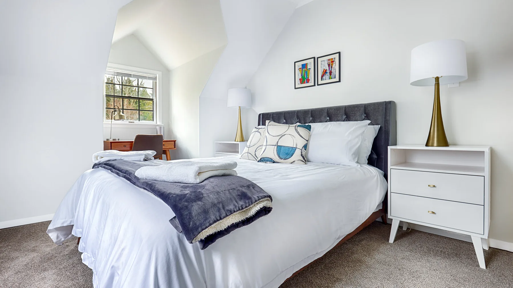 A bright bedroom with a neatly made bed and a window overlooking greenery.