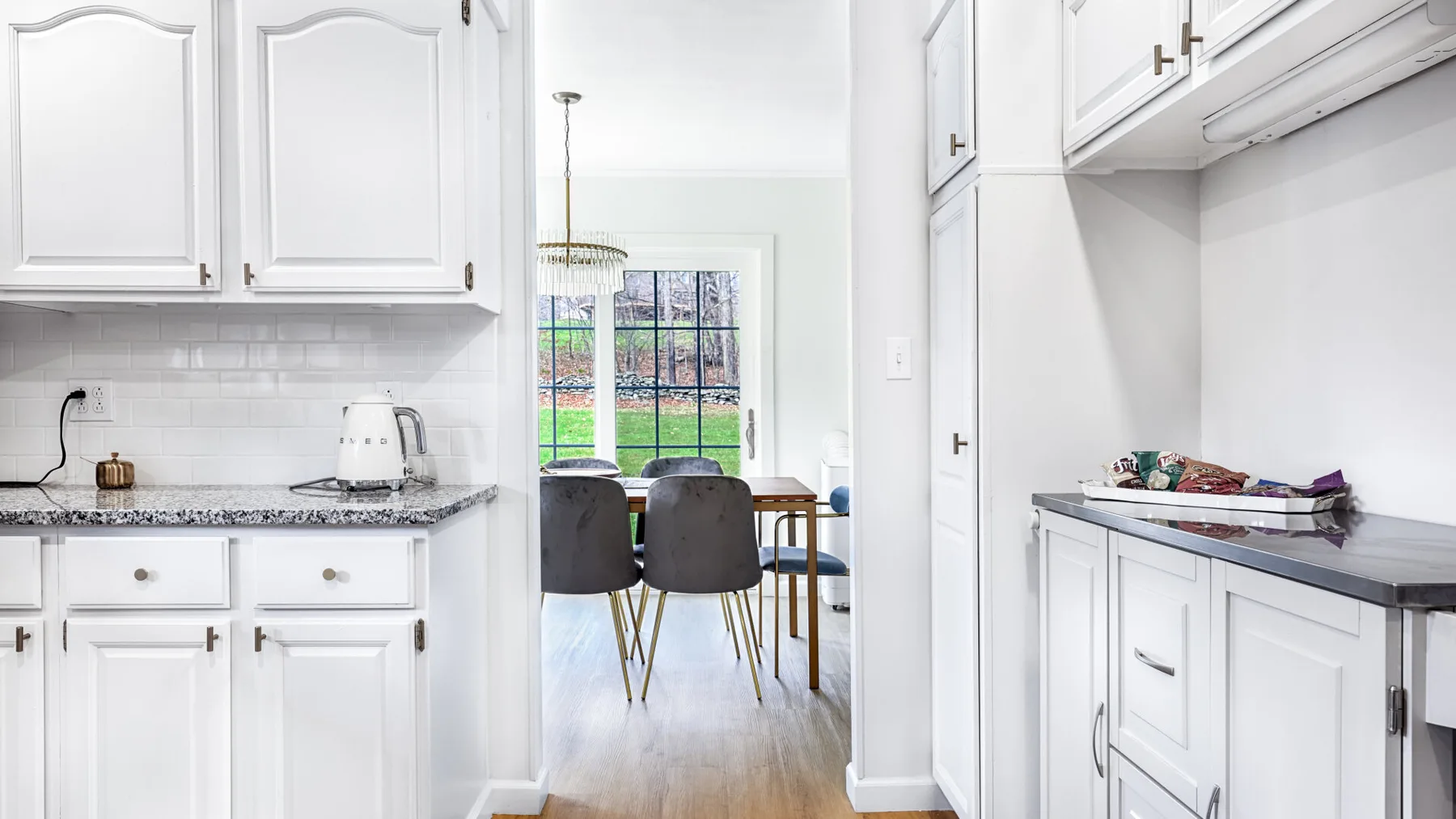 A bright white kitchen opens onto a dining area with a table and chairs.