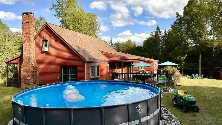 A red-sided house stands beside an above-ground pool and a grassy yard.