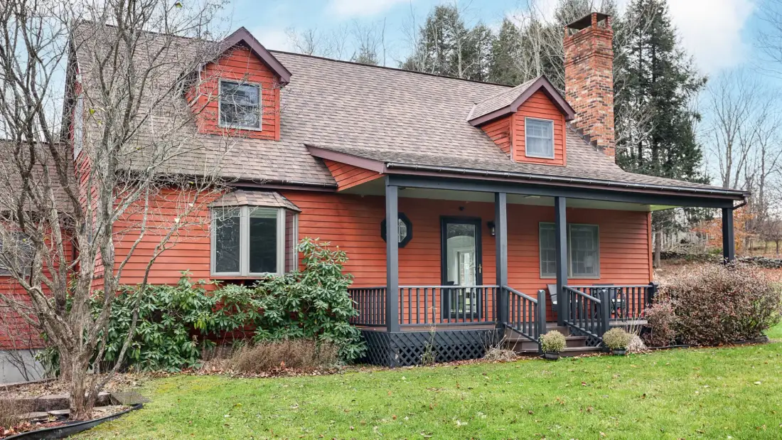 A red house with a covered porch and green lawn.