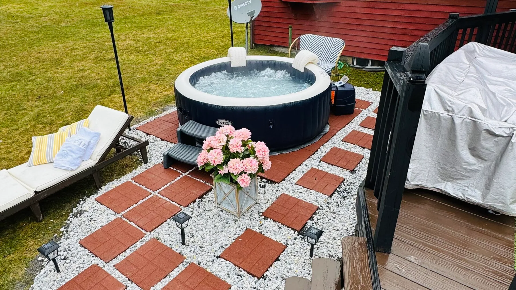 An outdoor hot tub sits on a stone patio beside a red-sided building.
