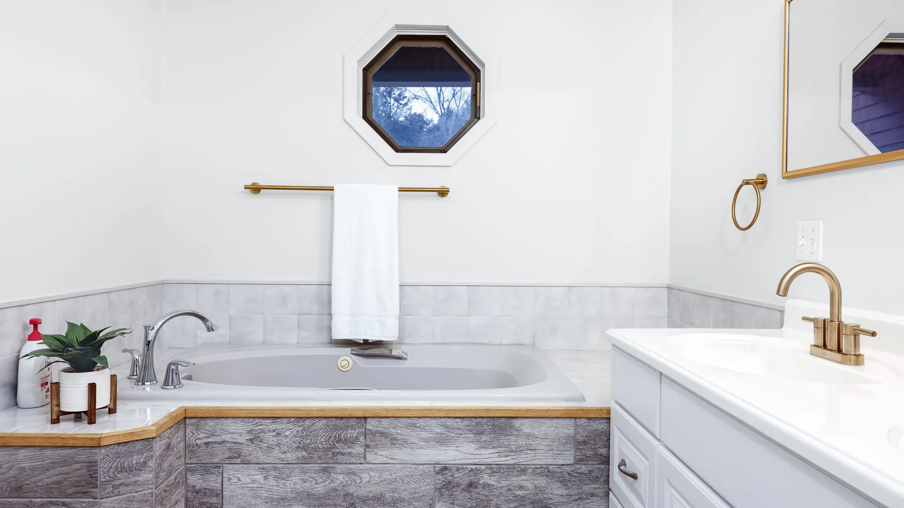 A bright bathroom with a built-in bathtub, vanity, and small window.