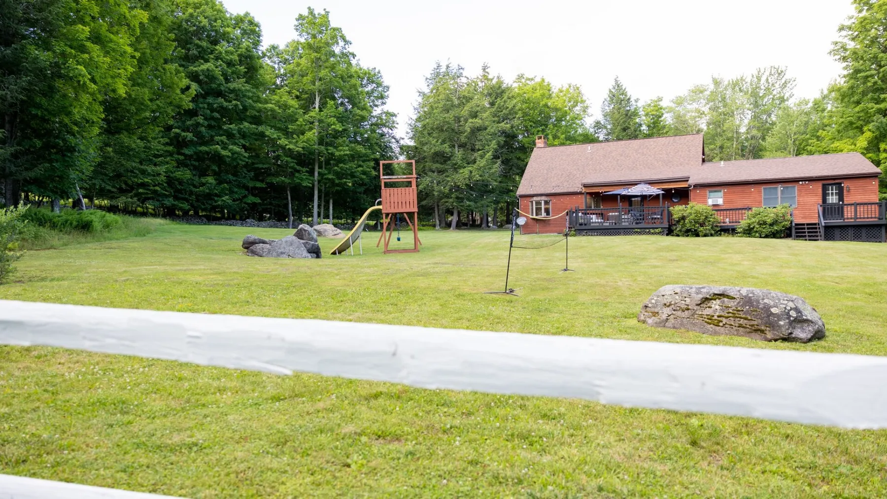 A grassy lawn with a wooden play structure and a red building in the background.