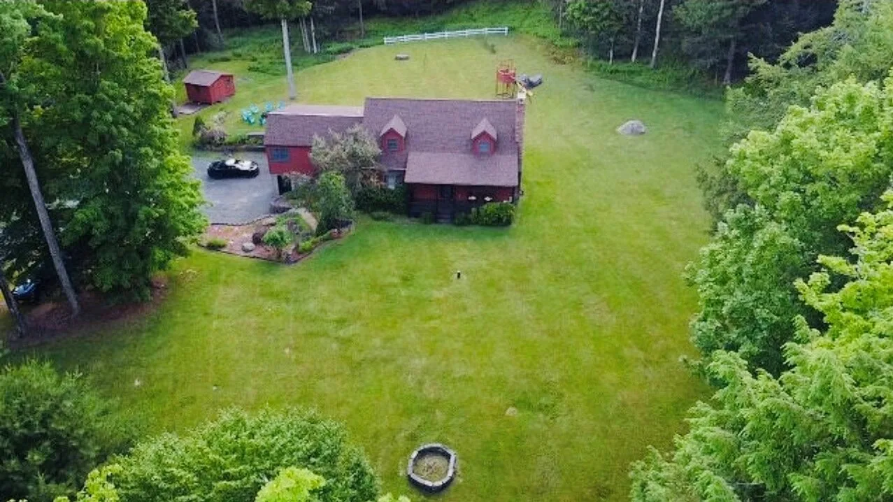 Aerial view of a house surrounded by a broad grassy lawn and trees.