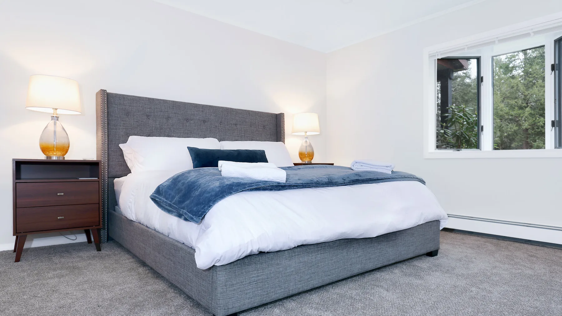 A bedroom with a large bed, bedside tables, and a window overlooking greenery.