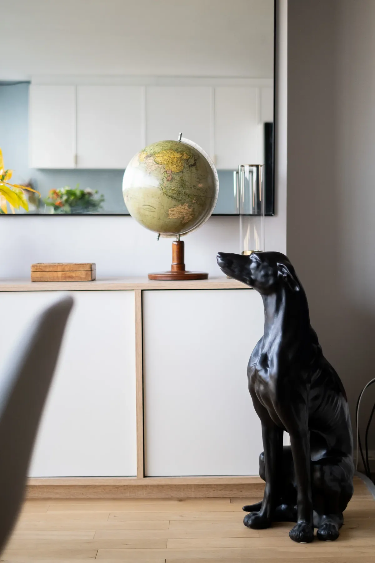 A black dog sits beside a globe in a bright kitchen.