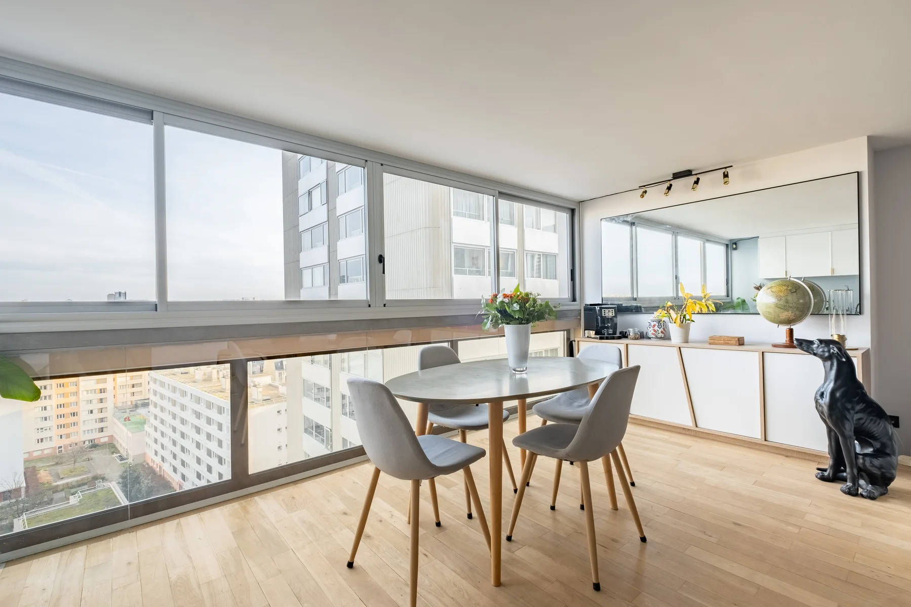 A bright dining area with a table and large windows overlooking nearby buildings.