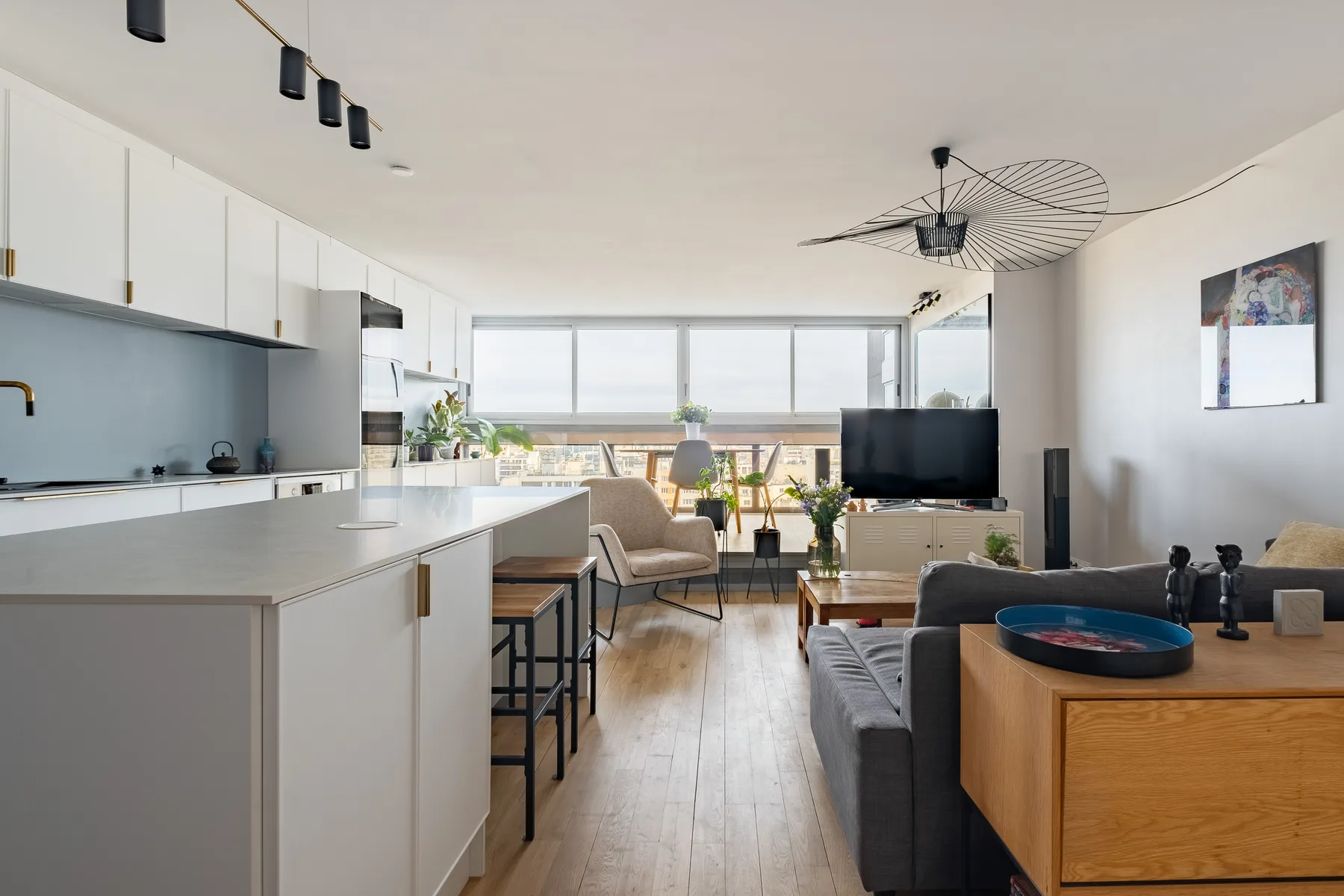 A bright open-plan living room and kitchen with large windows and seating.
