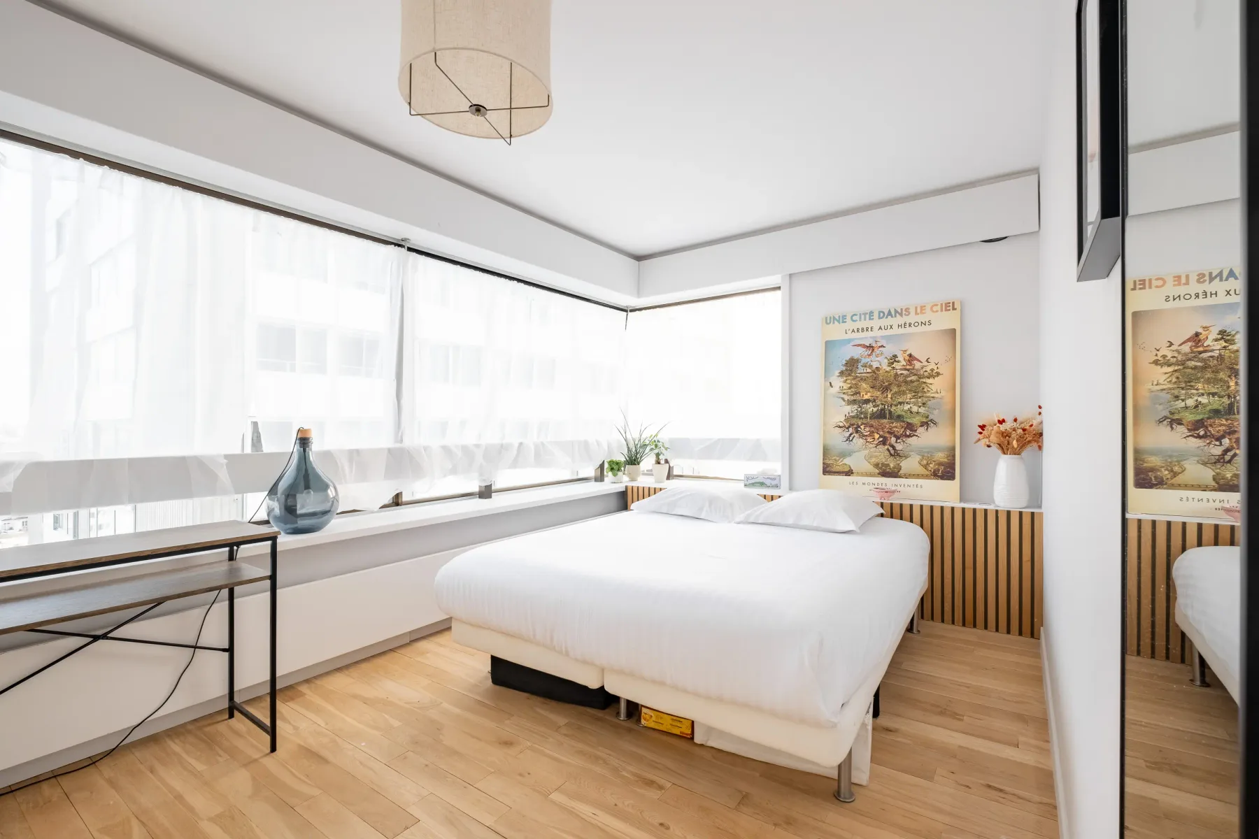 A bright bedroom with a white bed beside broad corner windows.