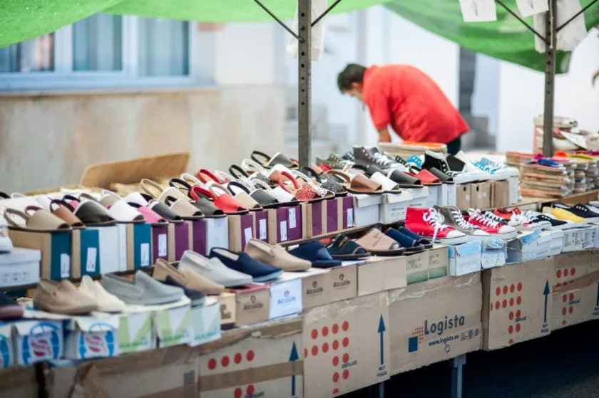 A market stall displays rows of shoes on boxes beneath a green canopy.