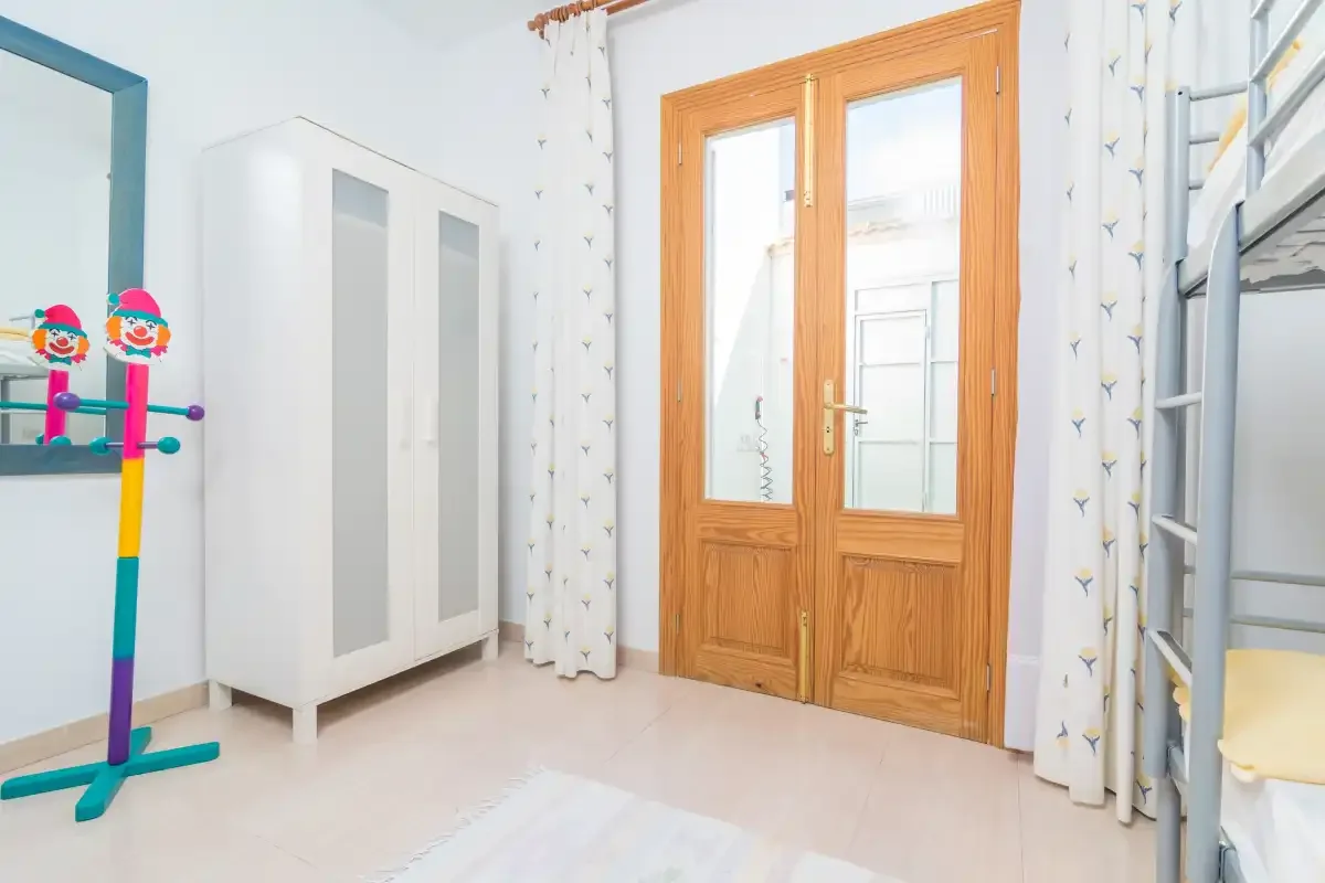 A bright bedroom with a wardrobe, wooden doors, and a metal bunk bed.