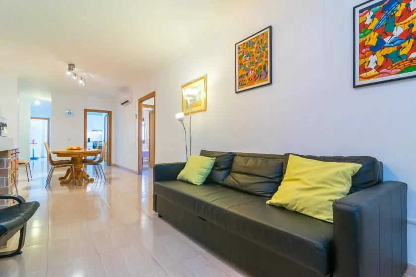 A living room with dark seating, colorful wall art, and a dining table in the background.