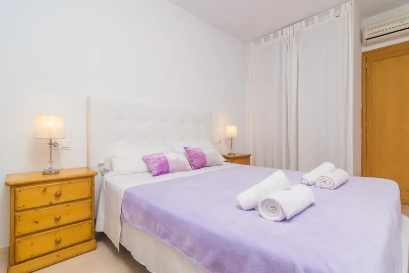 A bedroom with a lavender bedspread, bedside lamps, and white curtains.