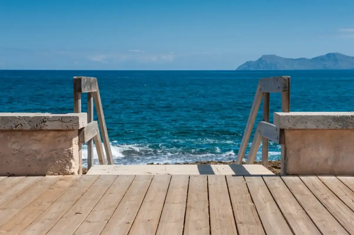 A wooden seaside deck leads to steps beside the blue sea.