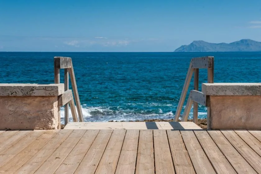 A wooden seaside deck opens toward the blue sea and distant islands.