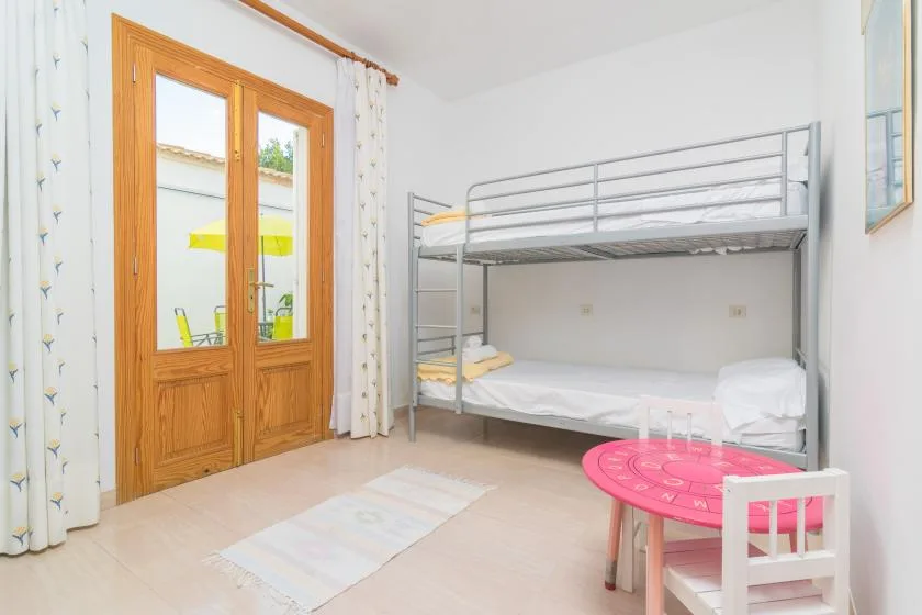 A bright bedroom with a metal bunk bed and a wooden glass-paneled door.